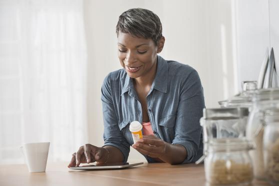 Woman holding medication bottle and looking at iPad.